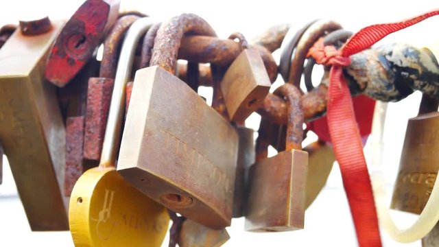 Pull back reveal away from many various rusty padlocks linked to chain walkway & ribbon blowing in wind.