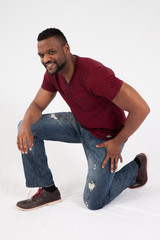 Happy Black man in jeans and red shirt, kneeling