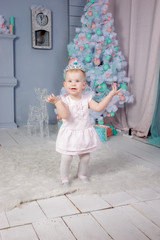 Portrait of a cute little european blond princess girl with a crown  in a beautiful dress in a studio decorated in the Christmas theme with toys and christmas tree