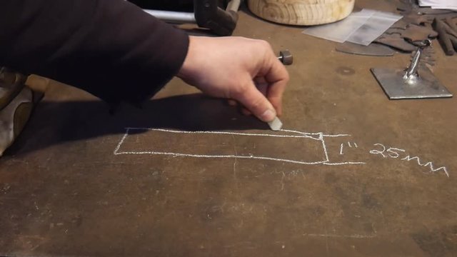 Man Drawing a Diagram in Soapstone on a Metalworking Workshop Work Table Showing a Diagram Drawn by Hand