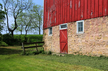 Beautiful springtime landscape with red barn. Sunny spring day view with old style stoned red barn and yard close up. Wisconsin, Midwest USA. Rural life and farming background. © Maryna