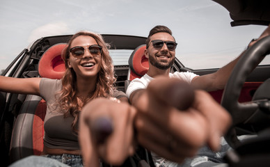 close up.young couple sitting in a convertible and pointing at you.
