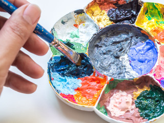 Artist hand mixing acrylic paint color with brush in plastic white art palette