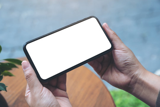 Mockup image of hands holding black mobile phone with blank desktop screen horizontally