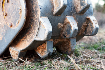 A closeup of a soil compactor on the back of a bucket on a track hoe.