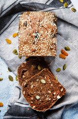 Whole wheat organic rye dark bread with pumpkin seeds, dried fruit, raisins and sesame seeds on gray towel on the kitchen table background, top view. Space for text vertical image