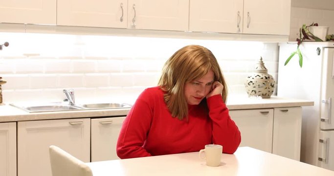 Portrait of a woman sitting in the kitchen  and having strong stomach ache  hands on abdomen
