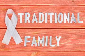 white awareness ribbon and inscription of iron letters: traditional family, lying on wooden...