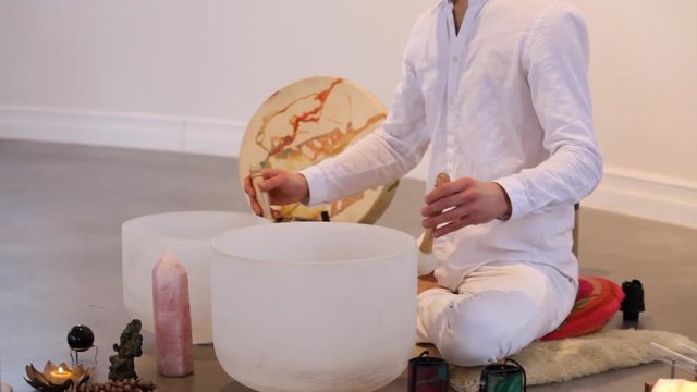 Man playing crystal bowls and singing. Traveling up on a man dressed in white playing crystal bowls and singing with various sacred objects displayed around him, side view