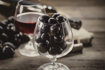 bunch of grapes in a wine glass. bottle and glass on a wooden table.