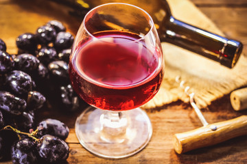 a glass of red wine, a bottle and a bunch of grapes on an old wooden kitchen table.