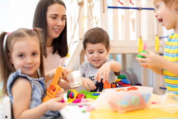 Little children engaged in playdough modeling at daycare. Kindergartener teaches kids molding