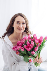 Portrait of young woman with pink tulips. White shirt