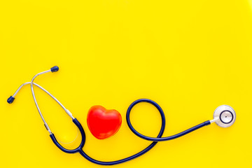 Heart health, health care concept. Stethoscope near rubber heart on yellow background top view copy space