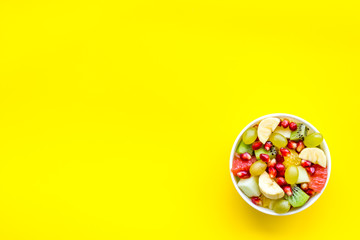 Light healthy breakfast or appetizer. Fruit salad with apple, kiwi and pomegranate in bowl on yellow background top view space for text