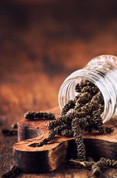 Fragrant long pepper spilling out of glass jar, vintage kitchen table background, selective focus