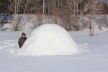 Man in warm clothes sitting by an igloo on a glade in the winter, Siberia, Russia