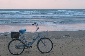 Old bicycle on the beach at sunset with storm sea and foam waves background.