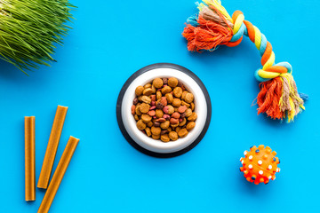 Pets accessories in home. Dog food in bowl and toys on blue background top view