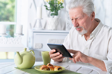  senior man using tablet while drinking tea
