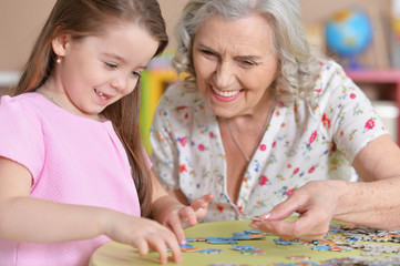 Cute little granddaughter and grandmother collecting puzzles