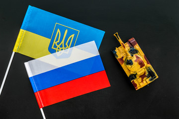 War, confrontation concept. Russia, Ukraine. Tanks toy near russian and Ukrainianflag on black background top view