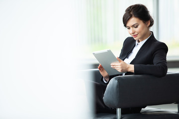 Stylish businesswoman sitting on sofa using tablet pc in the office.