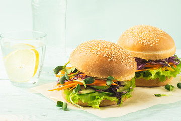 Appetizing burger from fresh sesame buns and raw vegetables and young sprouts blue light background.Healthy nutrition
