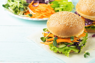 Appetizing burger from fresh sesame buns and raw vegetables and young sprouts on a blue light background. Vegetarianism.