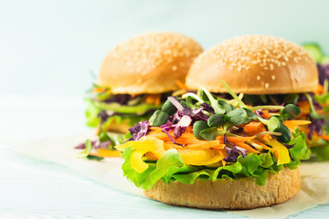 Appetizing burger from fresh sesame buns and raw vegetables and young sprouts on a blue light background. Vegetarianism.