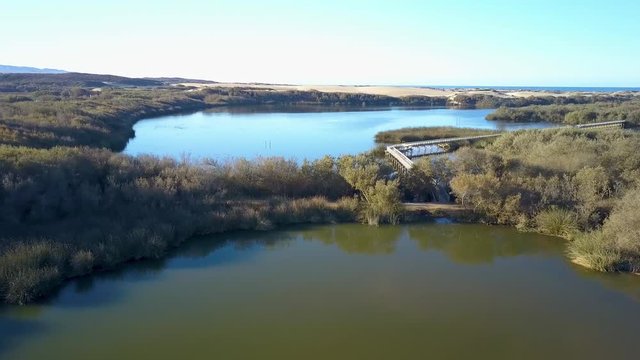 Scenic aerial drone view of lake with a boardwalk in Oso Flaco, located on the Central Coast of California, Santa Barbara County. These lakes are part of the Oceano Dunes.