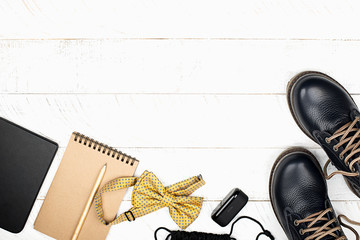 A set of a schoolboy boy: leather shoes, an e-book, a notebook for sketches, pencils, a snack, a banana, a bow tie, headphones in a case, a bag for things, shoes on a light background. Top view. Copy