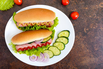 Tasty hot dogs with sausage grill, ketchup, mustard, lettuce, tomatoes on a white plate. The top view. Flat lay