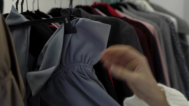Female hands touching different clothes/dresses hanging in the store closet. Girl is in the search of suitable item/dress. Woman attentive and careful