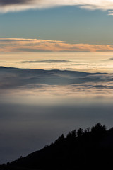 Beautiful view of Umbria valley (Italy) covered by a sea of fog at sunset, with beautiful warm colors and trees silhouettes in the foreground