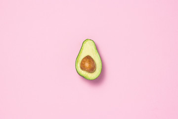 Half avocado on a pink background. Healthy eating concept. Flat lay, top view.