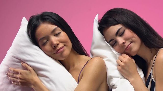 Beautiful multiethnic women sleeping on pillows against pink background, dreams