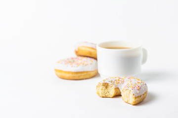 White Cup, coffee or tea with milk and fresh tasty donuts, sweet multicolored decorative candy on a white background. Bakery concept, fresh pastries, delicious breakfast, fast food.