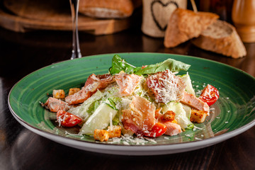 The concept of Italian cuisine. Caesar salad with salmon, lettuce mix, cherry tomatoes and parmesan cheese. A glass of white wine on the table. Serving dishes in the restaurant