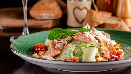 The concept of Italian cuisine. Caesar salad with salmon, lettuce mix, cherry tomatoes and parmesan cheese. A glass of white wine on the table. Serving dishes in the restaurant