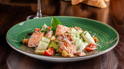 The concept of Italian cuisine. Caesar salad with salmon, lettuce mix, cherry tomatoes and parmesan cheese. A glass of white wine on the table. Serving dishes in the restaurant