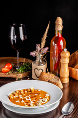 The concept of Italian cuisine. Pumpkin cream soup with orange flavor, chicken pieces, bread croutons and cream. A string of red wine on the table. Serving dishes in the restaurant