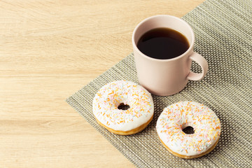 Tasty, sweet, fresh donuts and a cup with black coffee on the wooden background. Breakfast concept, fast food, coffee shop, bakery.