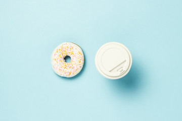 Fresh tasty sweet donut and paper cup with coffee or tea on a blue background. Fast food concept, bakery, breakfast,. Minimalism. Flat lay, top view.