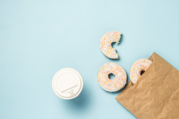 Paper cup with coffee or tea and Paper bag with Fresh delicious sweet donuts on a blue background. The concept of fast food, bakery, breakfast, sweets. Minimalism. Flat lay, top view.