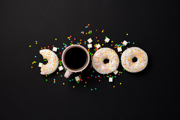 Delicious, sweet, fresh donuts, multicolored decorative candy, a cup of coffee on a black background. Concept of breakfast, fast food, coffee shop, bakery. Flat lay, top view.
