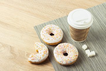 Delicious, sweet, fresh donuts and a paper cup with coffee or tea on a wooden background. Breakfast concept, fast food, coffee shop, bakery.