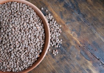 Organic brown lentils in terracotta bowl on an old weathered wooden table..