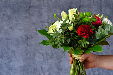 A male hand holding a bouquet of flowers. Colorful bouquet of flowers on a gray background