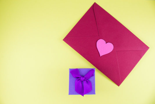 Dark red triangle envelope with large pink heart on yellow background with gift box Valentine's day or festive concept Letter or invitation inside closed envelope Minimalist concept with free space